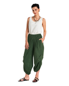 A woman modeling loose, draped olive green harem-style pants with a white sleeveless top and black sandals, standing against a plain white studio background.